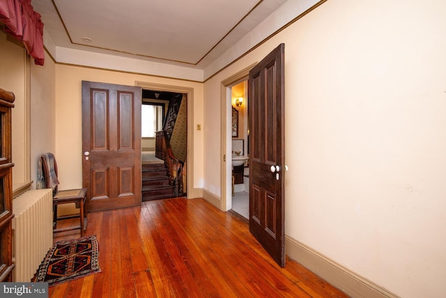 corridor featuring wood-type flooring, baseboards, radiator heating unit, and stairs