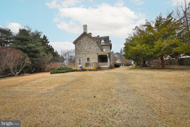 back of house featuring stone siding, a lawn, and a chimney