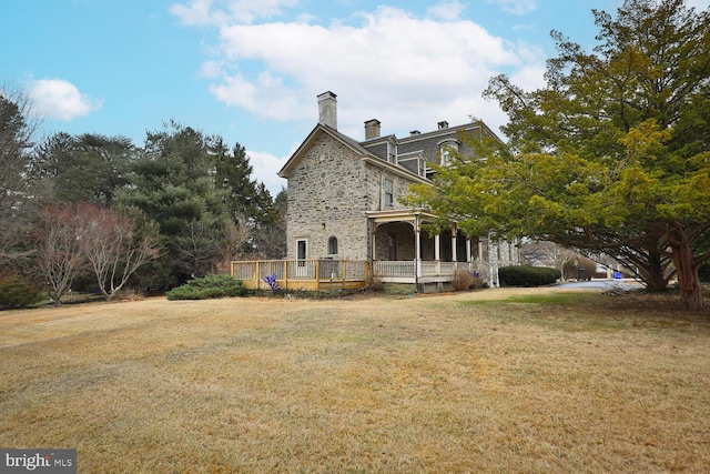 back of house featuring stone siding, a yard, and a chimney