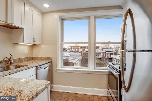 kitchen with baseboards, white cabinets, appliances with stainless steel finishes, light stone countertops, and a sink