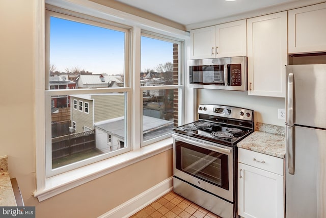 kitchen with baseboards, stainless steel appliances, light stone countertops, and white cabinets