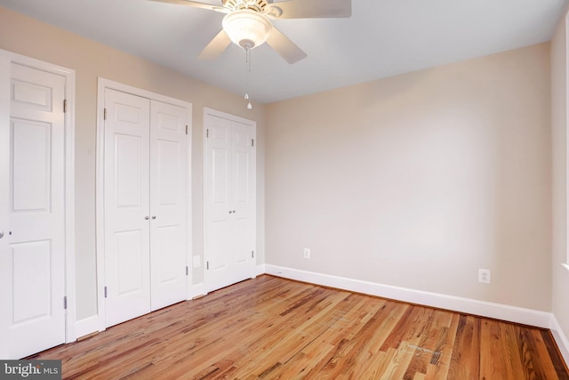 unfurnished bedroom with ceiling fan, light wood-style flooring, baseboards, and two closets