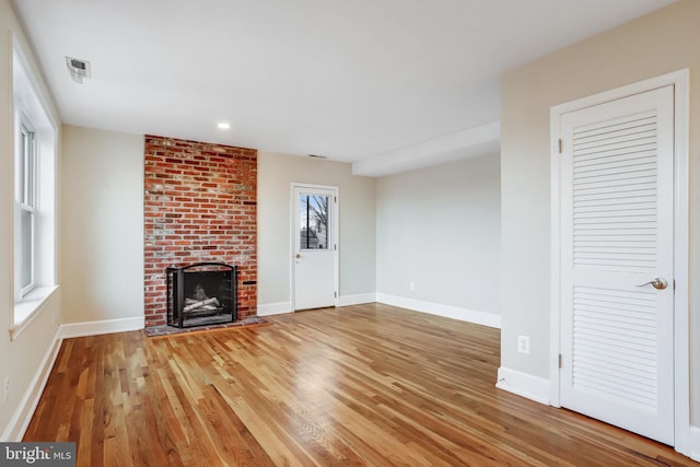 unfurnished living room with a brick fireplace, wood finished floors, visible vents, and baseboards