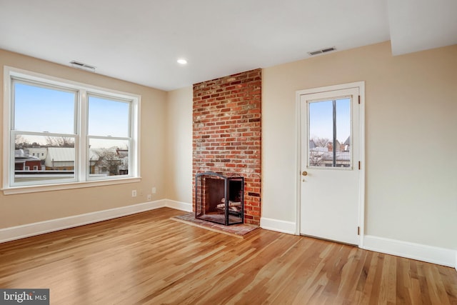 unfurnished living room featuring light wood-type flooring, a brick fireplace, visible vents, and a wealth of natural light