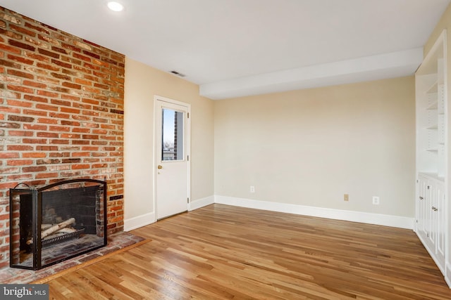 unfurnished living room featuring a brick fireplace, visible vents, baseboards, and wood finished floors