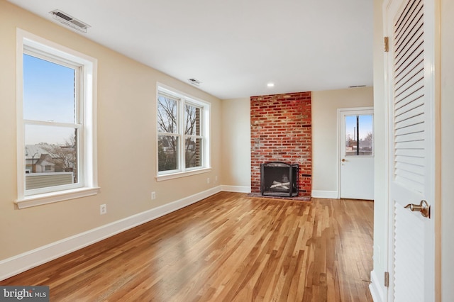 unfurnished living room with visible vents, baseboards, light wood-style flooring, a brick fireplace, and a wealth of natural light