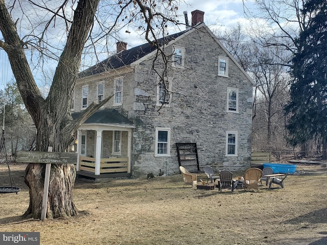 rear view of house featuring stone siding, an outdoor fire pit, and a chimney