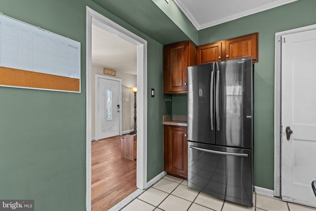 kitchen featuring baseboards, light tile patterned floors, freestanding refrigerator, and crown molding