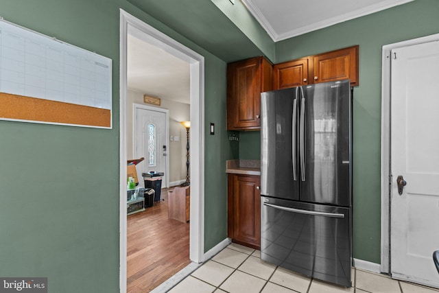 kitchen with light tile patterned floors, baseboards, brown cabinetry, ornamental molding, and freestanding refrigerator