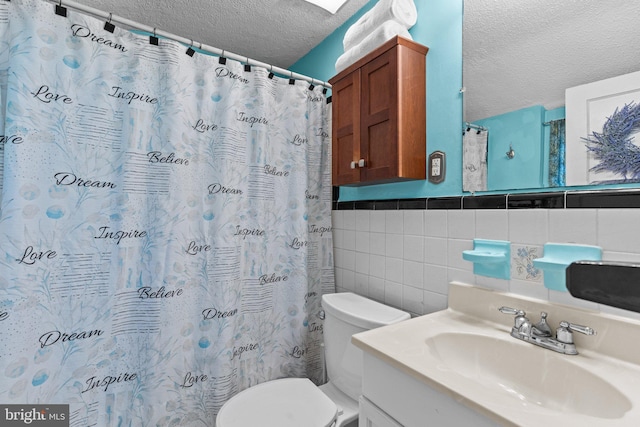 bathroom with a textured ceiling, curtained shower, toilet, vanity, and tile walls