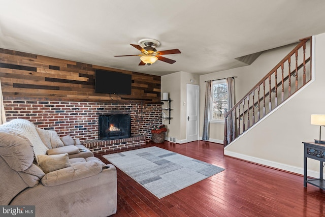 living room with hardwood / wood-style flooring, wood walls, a fireplace, a ceiling fan, and stairway