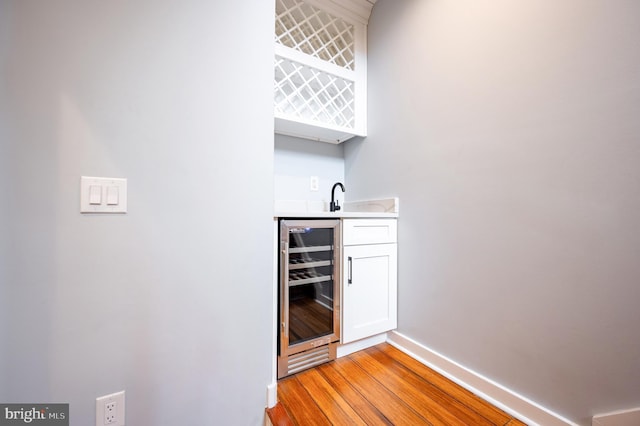 bar featuring light wood finished floors, beverage cooler, wet bar, and baseboards