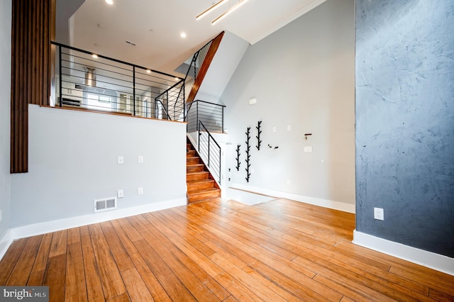 unfurnished living room featuring wood-type flooring, visible vents, baseboards, and stairs