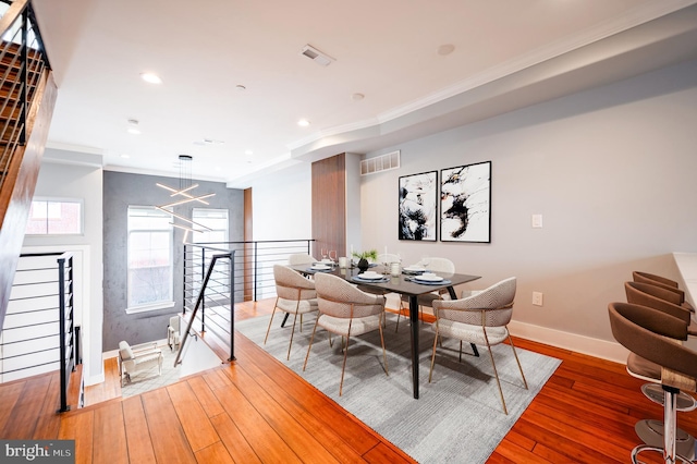 dining space with wood-type flooring, visible vents, and crown molding