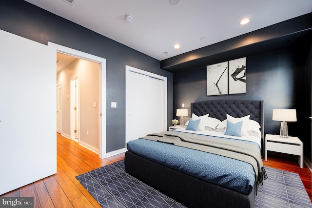 bedroom with hardwood / wood-style flooring, recessed lighting, visible vents, baseboards, and a closet