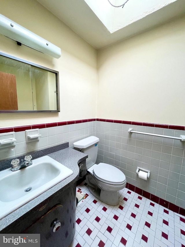 bathroom featuring tile patterned flooring, toilet, vanity, tile walls, and wainscoting