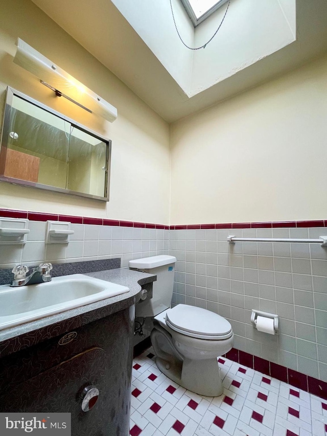 half bathroom featuring a skylight, toilet, a wainscoted wall, vanity, and tile walls