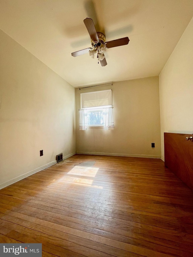 empty room with a ceiling fan, wood-type flooring, visible vents, and baseboards