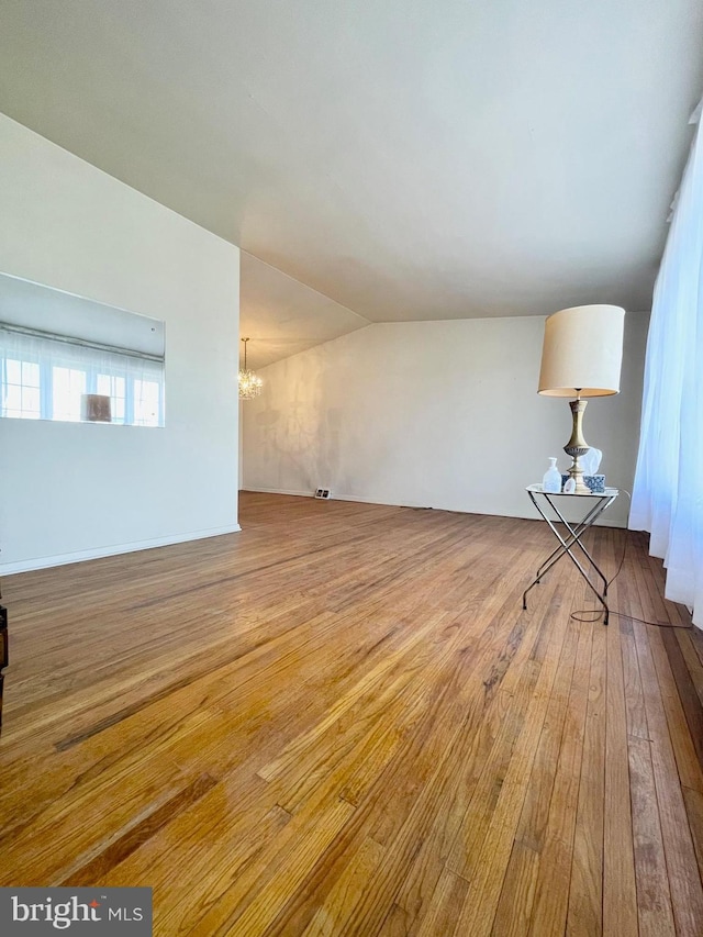 unfurnished living room featuring lofted ceiling, hardwood / wood-style flooring, and an inviting chandelier