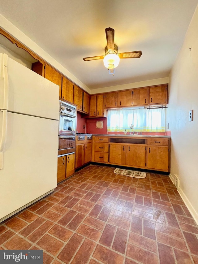 kitchen with brown cabinets, a warming drawer, freestanding refrigerator, a sink, and oven