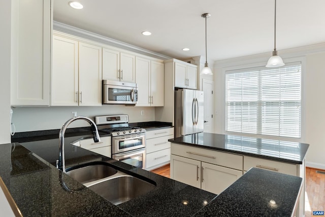 kitchen featuring crown molding, hanging light fixtures, appliances with stainless steel finishes, light wood-style floors, and a sink