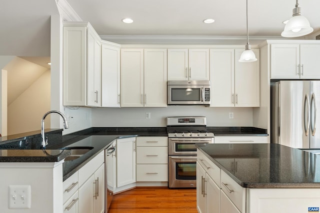 kitchen featuring light wood finished floors, decorative light fixtures, stainless steel appliances, white cabinetry, and a sink