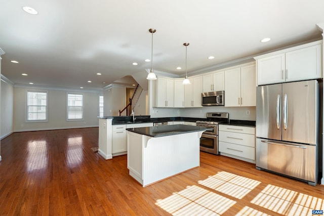 kitchen featuring crown molding, stainless steel appliances, dark countertops, white cabinetry, and hardwood / wood-style flooring