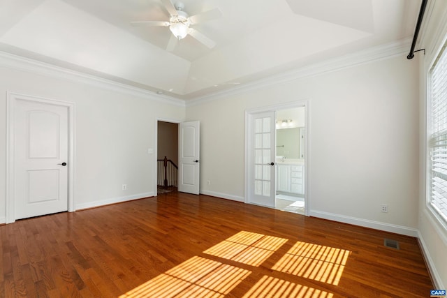 unfurnished bedroom featuring multiple windows, a tray ceiling, and wood finished floors