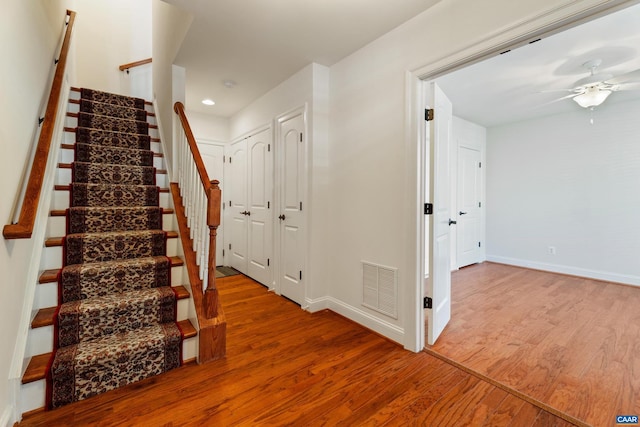 staircase with a ceiling fan, wood finished floors, visible vents, and baseboards