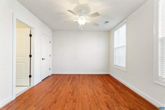 empty room featuring light wood-type flooring, visible vents, ceiling fan, and baseboards