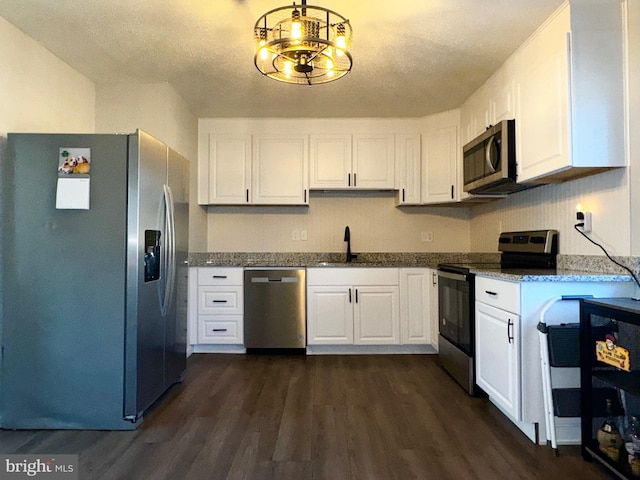 kitchen featuring stainless steel appliances, dark wood-style flooring, a sink, white cabinetry, and dark stone countertops