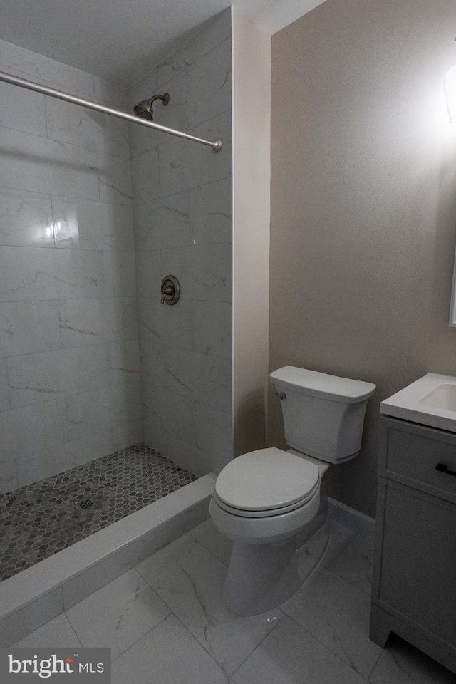 bathroom featuring toilet, marble finish floor, tiled shower, and vanity