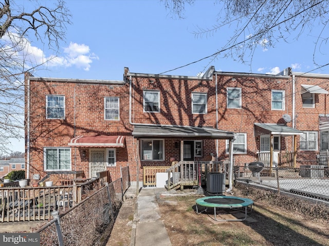 view of front of house featuring brick siding, a trampoline, and fence