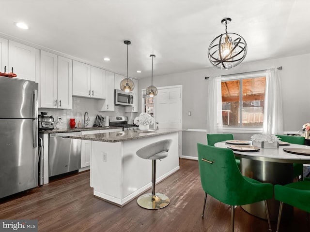 kitchen with dark wood-style floors, backsplash, appliances with stainless steel finishes, white cabinetry, and a kitchen island