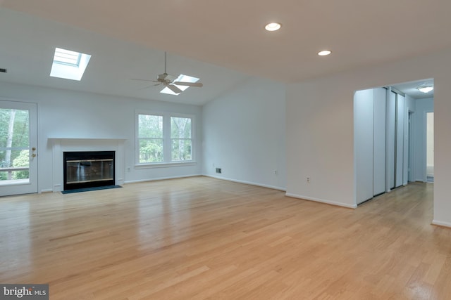 unfurnished living room featuring a skylight, a fireplace with flush hearth, light wood-style flooring, and recessed lighting