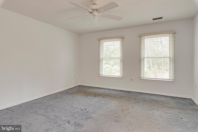 carpeted empty room with a healthy amount of sunlight, visible vents, ceiling fan, and baseboards