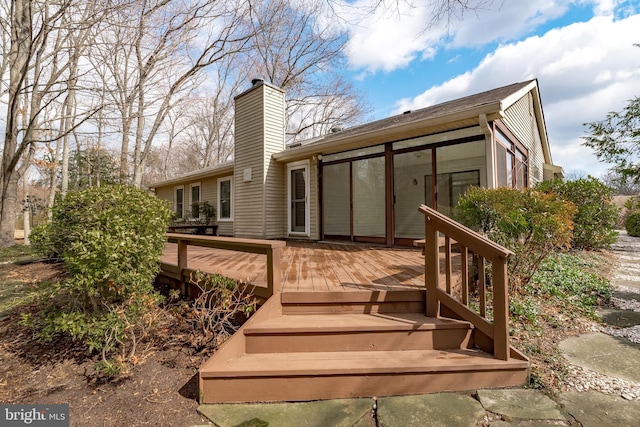 rear view of property featuring a sunroom, a chimney, and a wooden deck