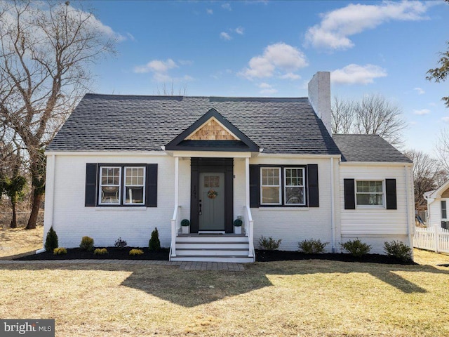 view of front of home featuring a shingled roof, a front yard, brick siding, and a chimney