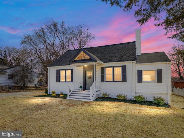 bungalow-style home featuring brick siding, fence, roof with shingles, a chimney, and a front yard