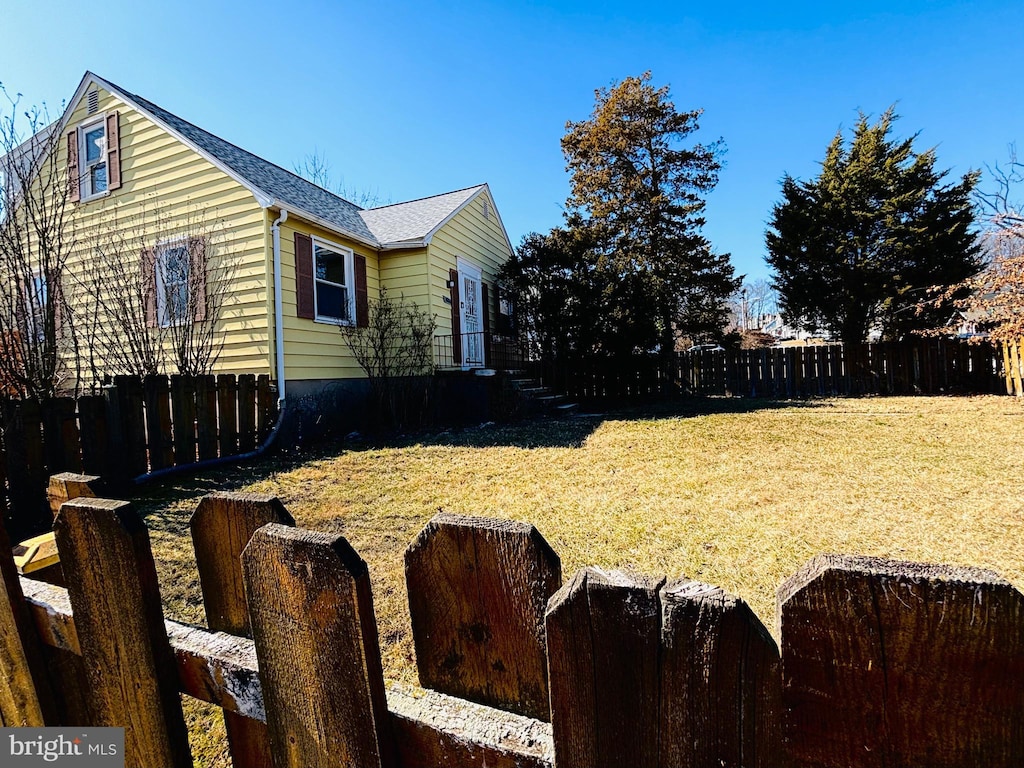 view of side of home featuring a shingled roof, fence, and a yard