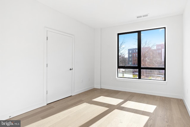 unfurnished room featuring plenty of natural light, wood finished floors, visible vents, and baseboards