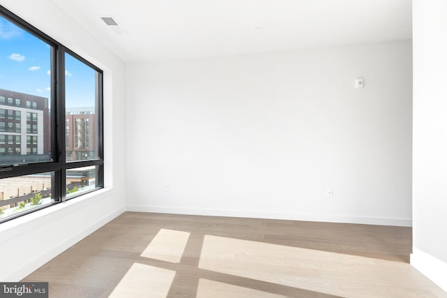 empty room featuring a healthy amount of sunlight, baseboards, visible vents, and wood finished floors