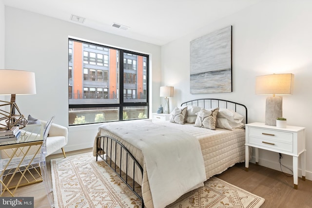 bedroom with wood finished floors, visible vents, and baseboards