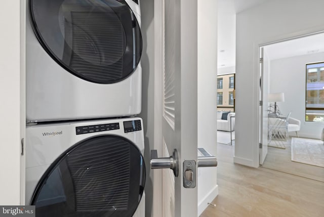 clothes washing area with stacked washer and dryer, wood finished floors, and laundry area