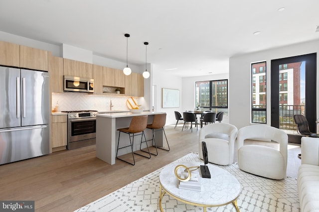 kitchen featuring light wood-style flooring, a breakfast bar, light countertops, appliances with stainless steel finishes, and tasteful backsplash