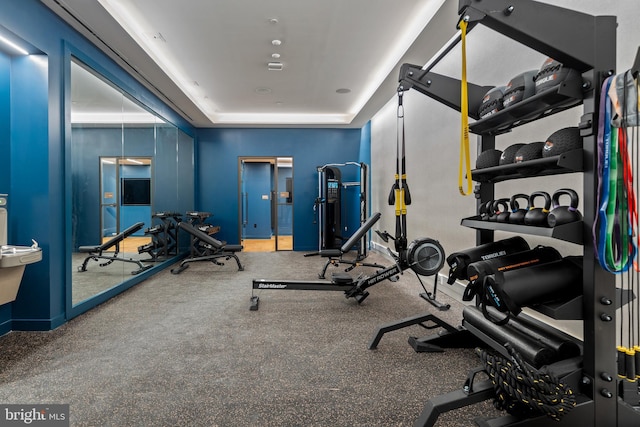 workout area featuring a tray ceiling and baseboards