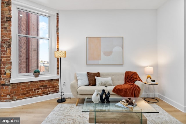 sitting room featuring brick wall, baseboards, and wood finished floors