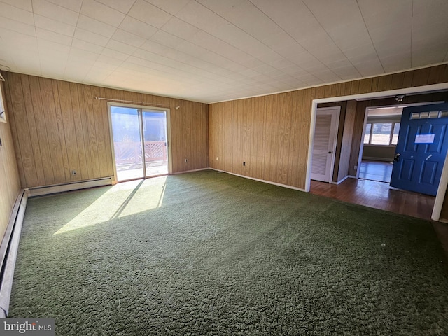 carpeted spare room featuring wooden walls and a baseboard heating unit