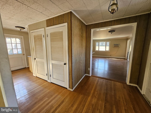 hall with baseboards, ornamental molding, hardwood / wood-style floors, a wall mounted air conditioner, and wood walls