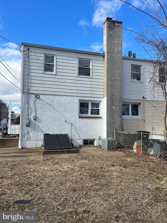 back of house with central AC unit, a chimney, and stucco siding